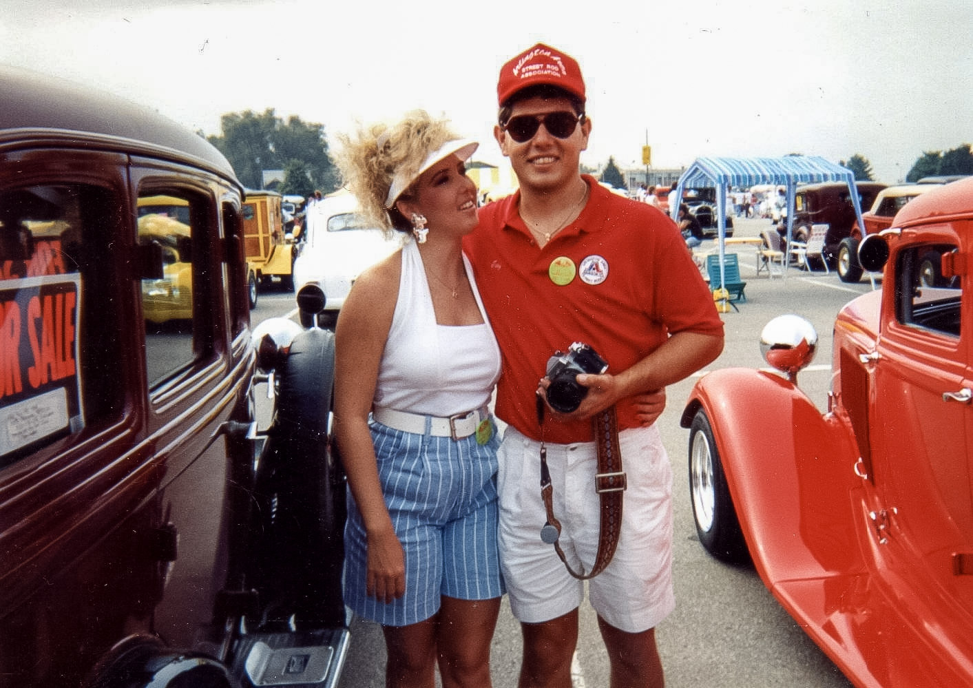 Troy Cryer holding a camera at a vintage car show, with two classic cars beside him